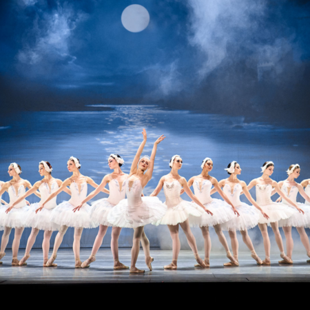 10 female ballet dancers in a line dressed in white with moonlit backdrop of a lake in mountains