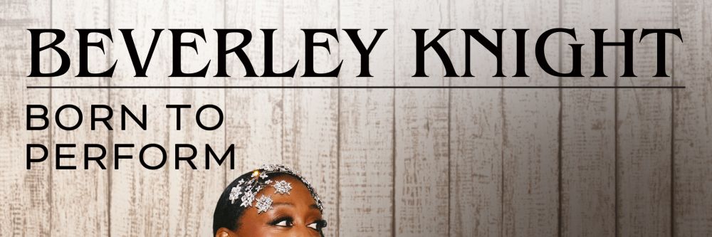 Beverley Knicght stood infront of a wood pannelled wall wearing a black ball gown with her hands on her hips staring to the right