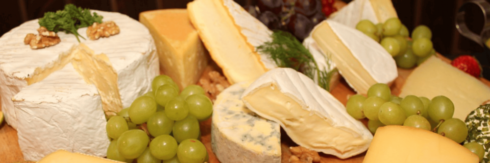 Cheese board including multiple types of cheese, green grapes, figs and strawberries